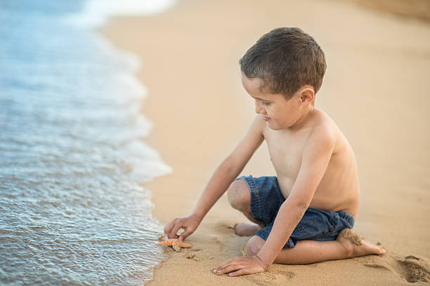 Young boy playing with a starfish on tropical hawaiian beach