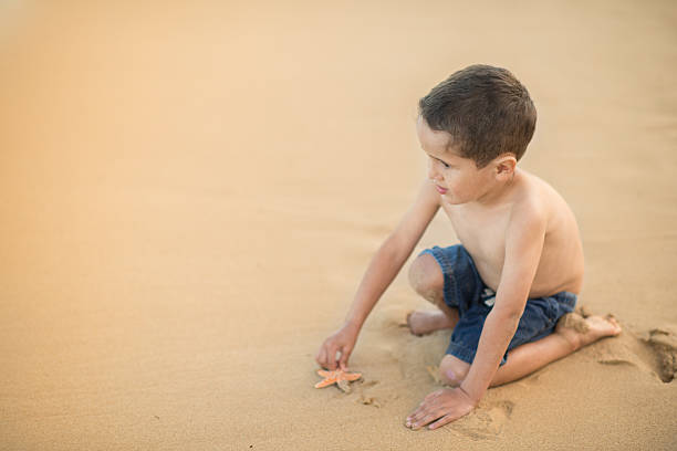 istock Young ethnic boy playing with starfish on tropical beach 534973311