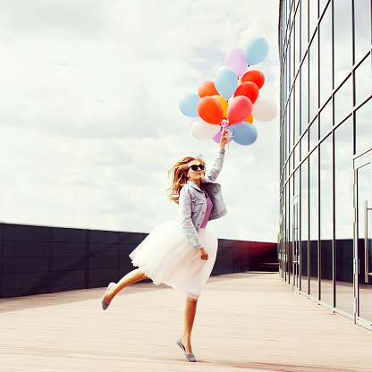 Jumping girl with colorful balloons in one hand. Warm sunny day. Outside.