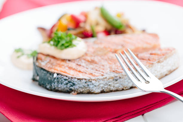 Grilled salmon steak served with fresh green vegetables on wooden table, salad dressing on dish. Healthy eating with clean food, balanced diet, nutritious meal and gourmet seafood cuisine.