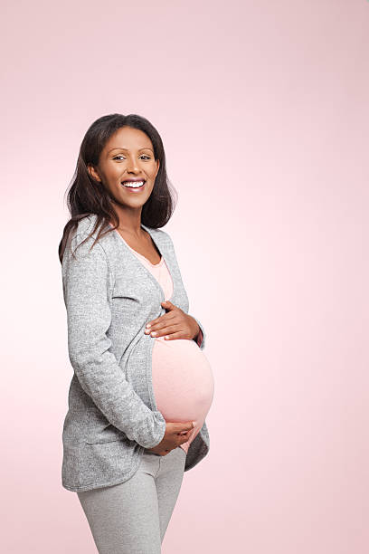 Pregnant woman. Smiling Ethiopian, 8 months pregnant woman with hands over tummy isolated on pink background. With copy space, cut out image. 8 months pregnant stock pictures, royalty-free photos & images
