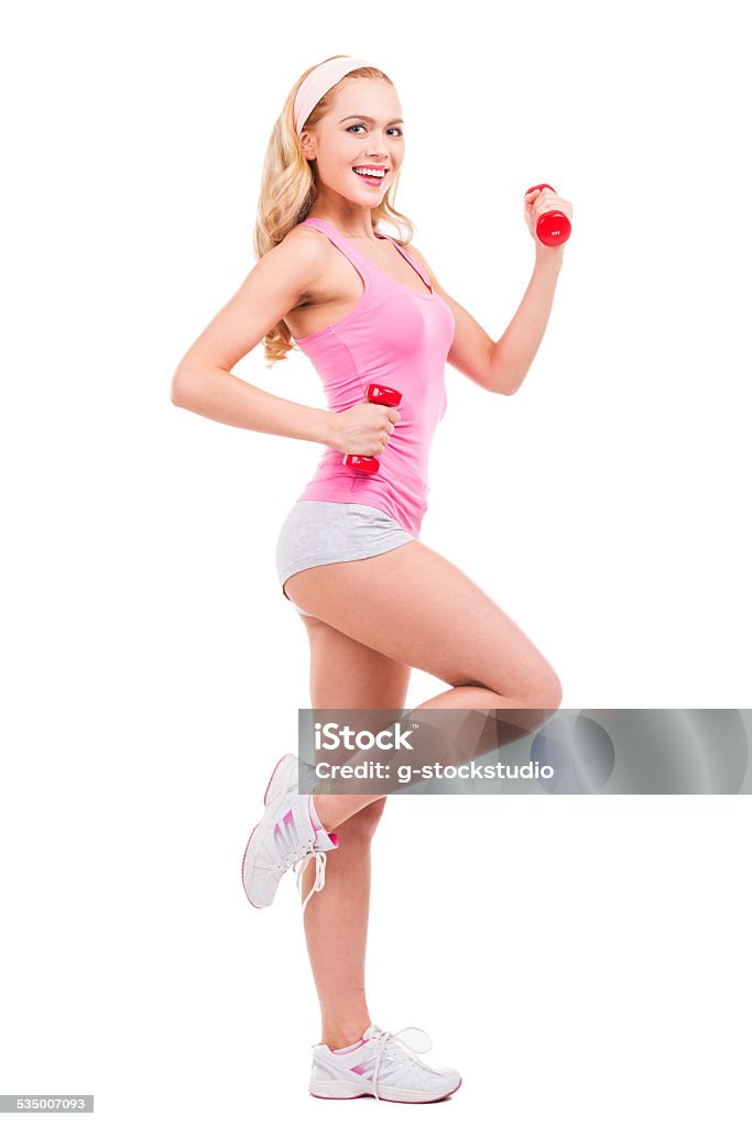 Keeping her body fit. Full length of beautiful pin-up blond hair woman in pink shirt exercising with dumbbells and smiling while standing isolated on white background 2015 Stock Photo