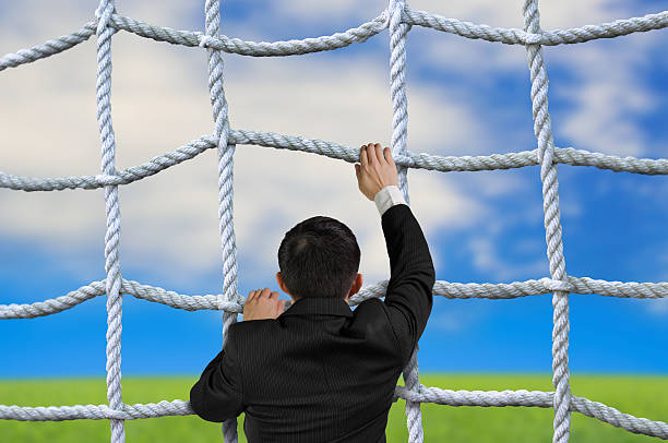 Businessman climbing crisscross rope net on sky cloud grass back