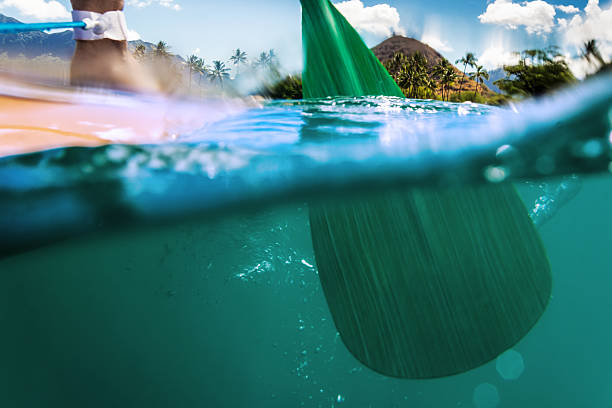 Paddling oar halfway submerged in ocean paddling across ocean surface