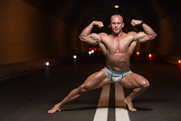 Bodybuilder Performing Front Double Biceps Poses In Tunnel Bodybuilder Performing Front Double Biceps Poses In Tunnel body adornment rear view young men men stock pictures, royalty-free photos & images