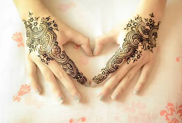 Beautiful drawing henna on female hands with mehndi decoration in heart shape. Love Concept.