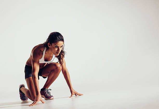 Focused woman ready for a run Female athlete in position ready to run over grey background. Determined young woman ready for a sprint. running motion stock pictures, royalty-free photos & images