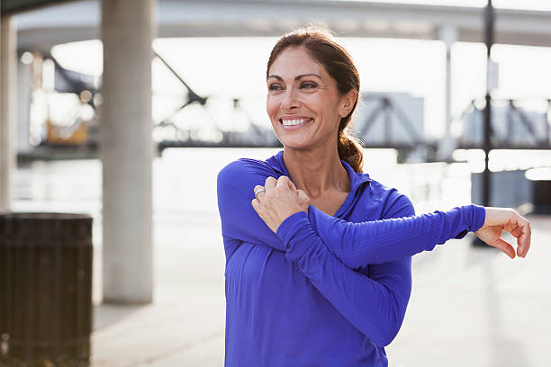 donna matura allungamento durante un po'di jogging sul lungomare - spalla giuntura foto e immagini stock