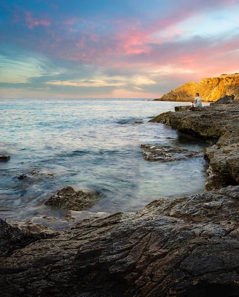 Young woman sitting on rocks and looking at the sea