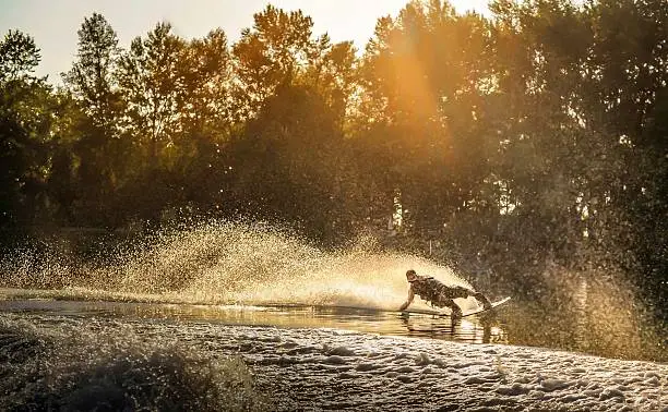 Wakeboarder sliding on a lake with sunset and forest behind.