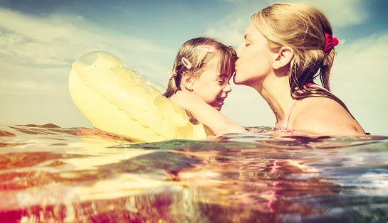 Mother and daughter are enjoying themselves in the sea. Real family, genuine emotions. Water splashes on the camera. Vintage toned, format 16:9. AdobeRGB profile.
