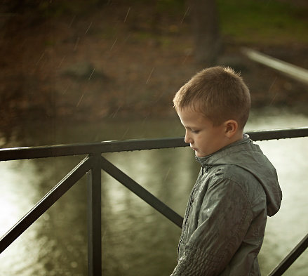 Sad boy standing outside under the rain