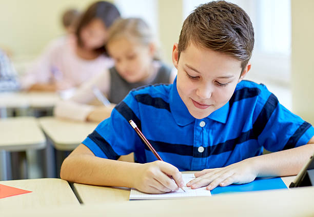 group of school kids writing test in classroom education, elementary school, learning and people concept - group of school kids with pens and notebooks writing test in classroom primary school exams stock pictures, royalty-free photos & images