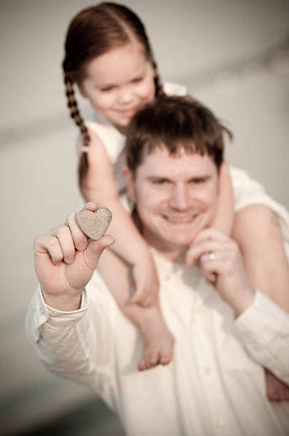 Father Holding Heart-Shaped Rock with Daughter on Shoulders
