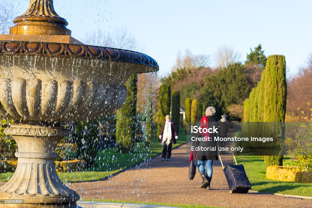 Regent's Park in Borough of Camden, London London, England - December 28, 2014: People strolling through the park of Regent's Park in Camden. In the foreground is a woman walking past a fountain with a suitcase.  Regent's Park Stock Photo