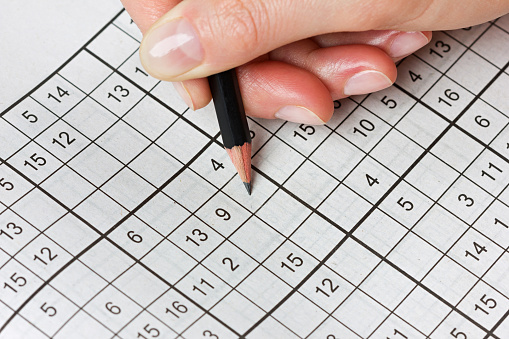 woman hand holding a pencil and solves crossword sudoku, popular puzzle game with numbers
