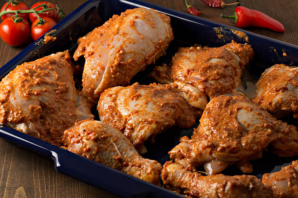 Marinating Chicken A high angle extreme close up shot of a blue metal tray with several pieces of chicken marinating in a spicy homemade African Harissa paste/sauce, the chicken will marinate for 24 Hours before being baked in the oven. The tray is framed by several ripe tomatoes and spicy chili peppers. marinated photos stock pictures, royalty-free photos & images