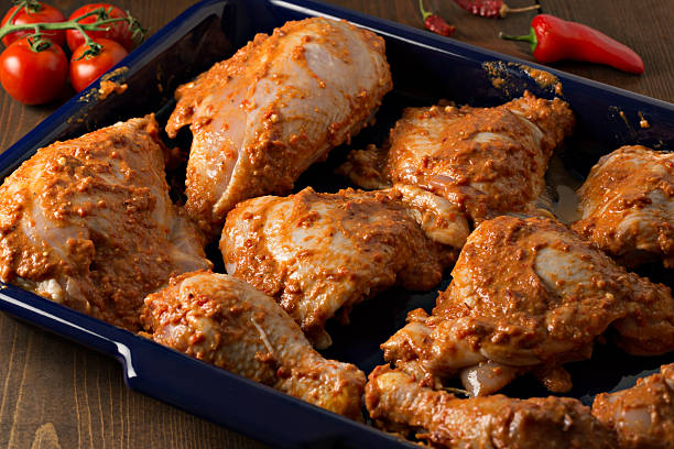 Marinating Chicken A high angle extreme close up shot of a blue metal tray with several pieces of chicken marinating in a spicy homemade African Harissa paste/sauce, the chicken will marinate for 24 Hours before being baked in the oven. The tray is framed by several ripe tomatoes and spicy chili peppers. marinade stock pictures, royalty-free photos & images