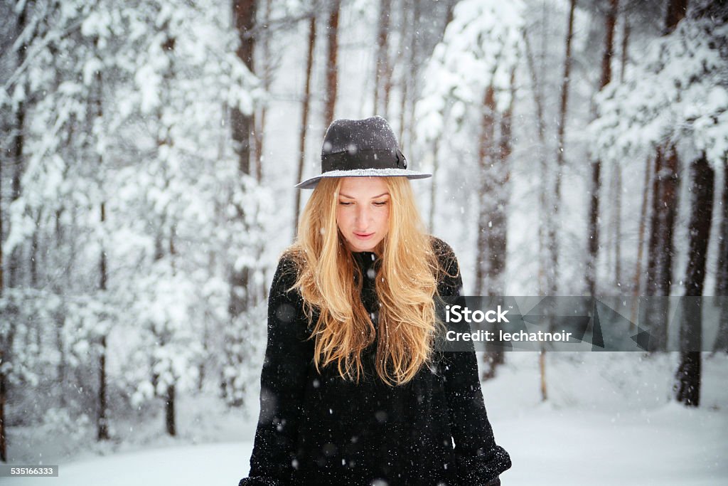 Walking in the snowy forest Portrait of a young blonde fashion model walking in the snowy forest, wearing warm black clothing and a hat. One Woman Only Stock Photo