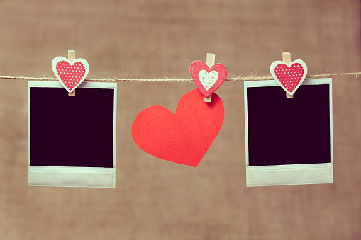 Two polaroid photo frames and heart for valentines day hanging on vintage background with vintage toning