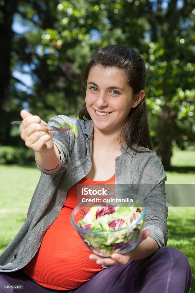 young pregnant offering salad pregnant young woman with orange shirt offering salad sitting at a park in Madrid Spain Europe 2015 Stock Photo