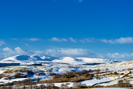 A remote area of Dumfries and Galloway in south west Scotland with snow covering fields and distant hills. Photographed on a bright winters day.