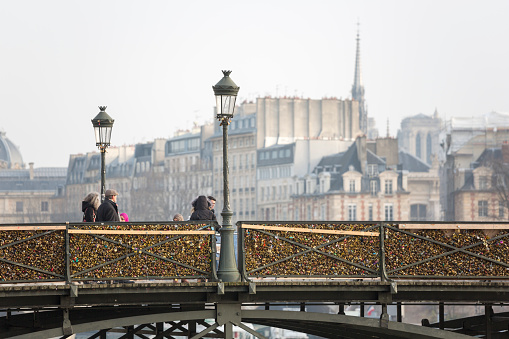 Paris, France - January 23, 2015: Padlocks on the Passerelle des Arts Bridge, or Pont des Arts Bridge, can be seen by passersby as they stroll.  Locks are sold by street vendors to people to attach to the bridge as a celebration of their love.  