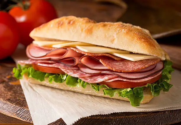 A delicious sandwich with cold cuts, lettuce, tomato, and cheese on fresh ciabatta bread.
