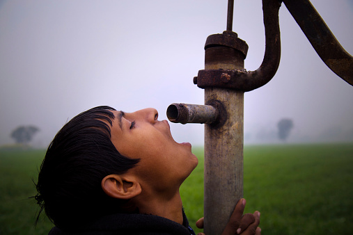 Teenage Indian Boy Drinking Water Near Green Field Outdoor.