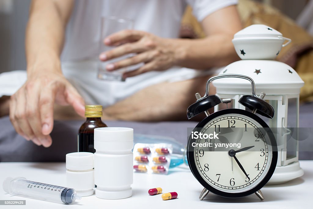 Asian Man in bed with tablets and water Asian Man in bed with tablets and water suffering insomnia, hangover and headache at night 2015 Stock Photo