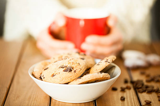 Closeup of cookies and a woman, holding a red mug at a wooden table.