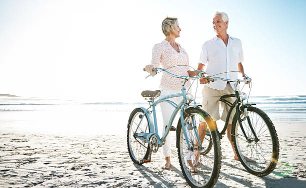 êtes-vous prêt à agir comme un enfant à nouveau ? - senior couple cycling beach bicycle photos et images de collection