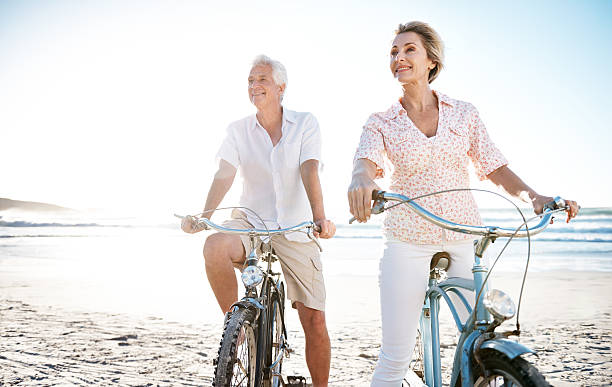 il y a toujours du temps pour se divertir - senior couple cycling beach bicycle photos et images de collection