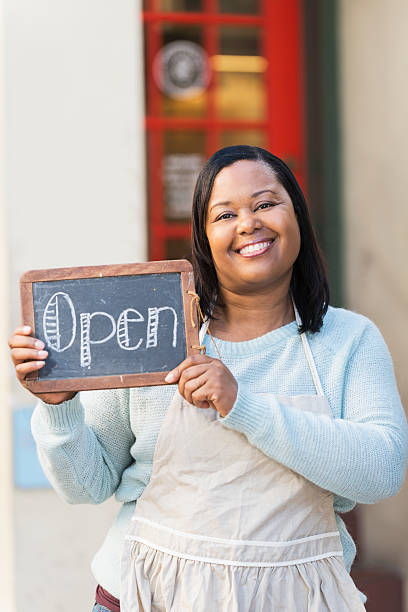 istock Black woman wearing apron holding OPEN sign 535259907