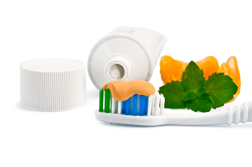 Toothbrush with toothpaste orange, a sprig of green mint, orange slices, a tube and cap isolated on white background