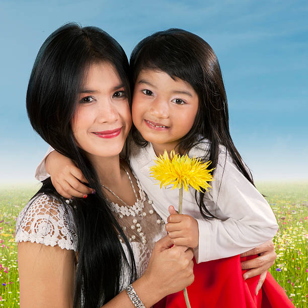 Portrait of lovely woman holding flower with her daughter while smiling at the camera