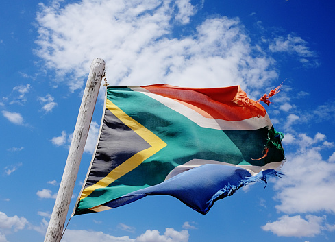 Rather battered and frayed South African flag billowing in the wind against a cloud-strewn sky. 20 years of democracy has left its mark.