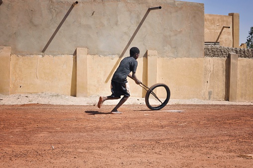 African child playing in the street bare foot with a bicycle wheel.