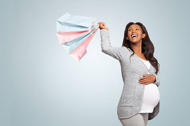 Excited pregnant woman with shopping bags. Side view of a beautiful 8 months pregnant woman, Swinging shopping bags pink and blue shopping bags, Stroking her belly. isolated on blue background, with copy space. 8 months pregnant stock pictures, royalty-free photos & images