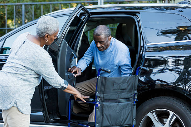 Disabled senior man getting from car to wheelchair A disabled senior African American man is getting out of a car, into his wheelchair.  His wife is helping him, holding the door open.  Focus on man. disabled sign stock pictures, royalty-free photos & images