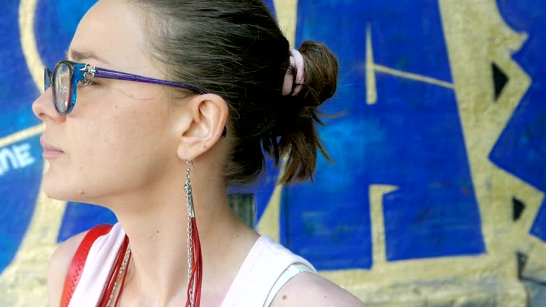 Slow motion shot of a young adult woman standing in front of graffiti wall and looking around