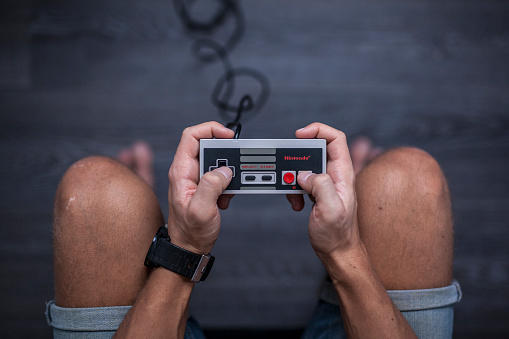 Gothenburg, Sweden - January 31, 2015: A shot from above of a young man's hands using a Nintendo game controller, a remote controller for the Nintendo Entertainment System developed by Nintendo Co., Ltd. in the 1980s. Natural lighting. Shot on a grey wooden background.