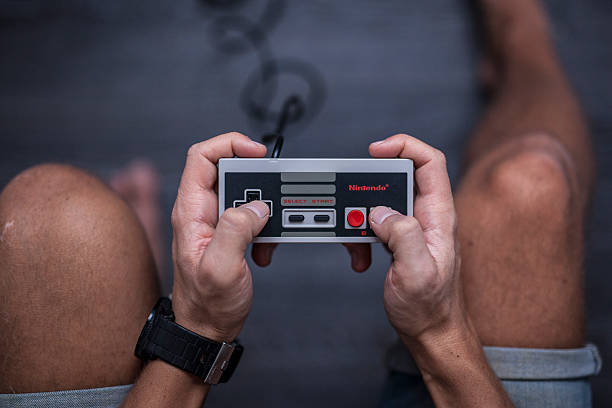 Nintendo Entertainment System - Video Game Controller Gothenburg, Sweden - January 31, 2015: A shot from above of a young man's hands using a Nintendo game controller, a remote controller for the Nintendo Entertainment System developed by Nintendo Co., Ltd. in the 1980s. Natural lighting. Shot on a grey wooden background. brand name games console stock pictures, royalty-free photos & images