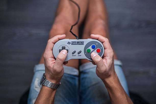 SNES Controller - Super Nintendo Game Controller Gothenburg, Sweden - January 31, 2015: A shot from above of a young man's hands using a Super Nintendo game controller, a remote controller for the Super Nintendo Entertainment System developed by Nintendo Co., Ltd. in the early 1990s. Natural lighting. Shot on a grey wooden background. brand name games console stock pictures, royalty-free photos & images