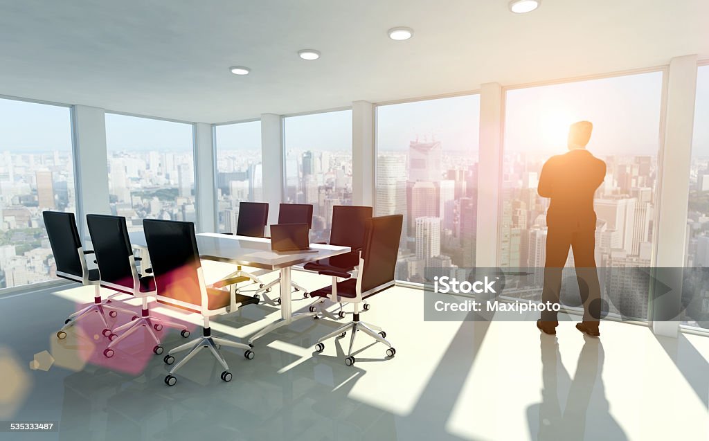 Businessman looking outside window, thinking about opportunities Silhouette of one business man in front of a window inside a modern office with a conference desk: warm sunrise light fills the room creating lens flares. Looking outside: meditating, planning about future opportunities. Outside the windows the skyline of a city with skyscrapers is visible.  Window Stock Photo