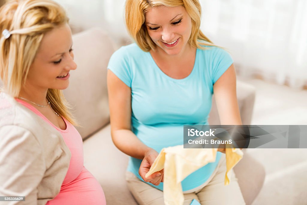 Do you like it? Two happy pregnant women enjoying at home while looking at baby clothes. 2015 Stock Photo