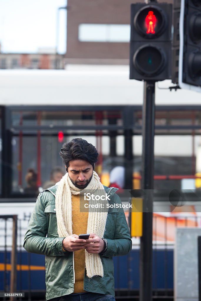 Using Mobile Telephone While Crossing A Road Young male looking at his mobile telephone while crossing a road. Bus Stock Photo