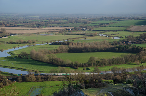 A commuter train passes by the Ouse valley and the River Ouse viewed from Offham Hill on the edge of the South Downs, England