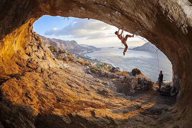Young woman lead climbing in cave, male climber belaying. Kalymnos island, Greece.