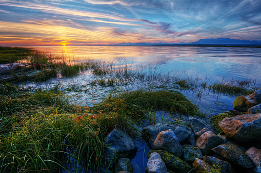 Relaxing summer river sunset with green grass and distant mountains
